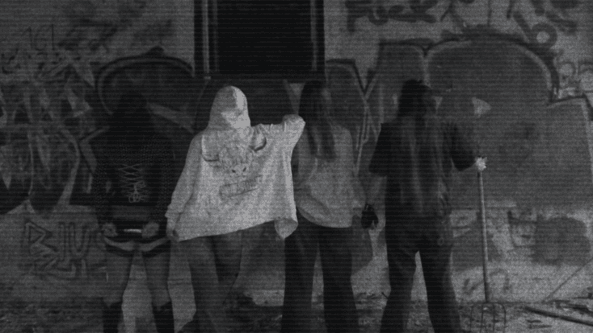 Die Band von hinten vor einer Graffitiwand, in der Mitte ein weißer Hoodie mit Stierkopf